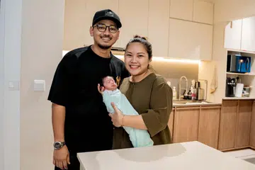 Encik Imam Wahyudi Bambang Budiono dan Cik Ira Wahyuni Bambang Suwarno bergambar bersama bayi mereka, Izy Windrawan. Mereka berdiri di dapur rumah di mana Cik Ira melahirkan Izy dalam posisi berdiri tanpa bantuan perbuatan.
