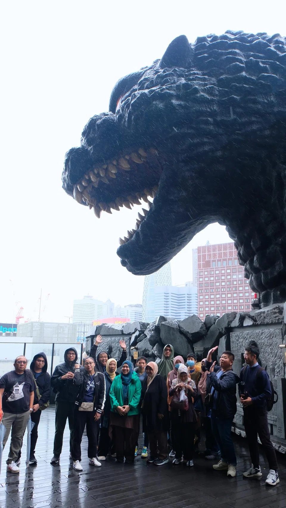 DEKATI GODZILLA: Sedang pelancong Singapura bergambar di depan replika  reptilia ikonik Godzilla, terasa angin kencang tempias taufan di situ.