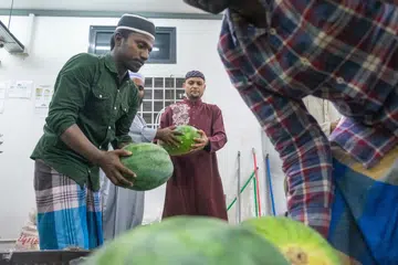 Seorang pekerja migran Bangladesh, Encik Jahidul Islam (tengah), yang tinggal di asrama ASPRI-Westlite Papan, membeli tembikai di kedai asrama untuk juadah berbuka puasa bersama rakan senegaranya.