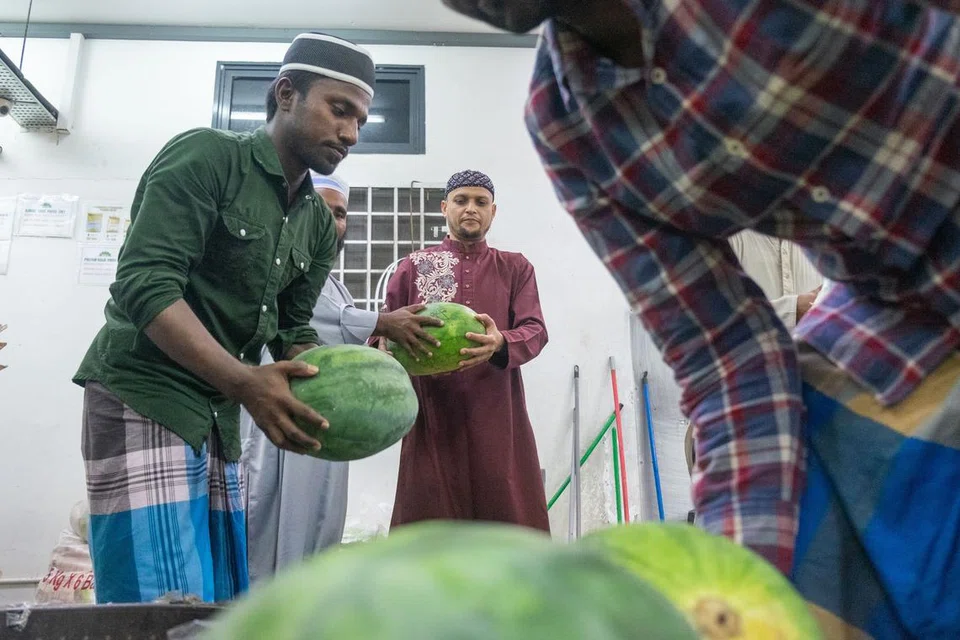 Seorang pekerja migran Bangladesh, Encik Jahidul Islam (tengah), yang tinggal di asrama ASPRI-Westlite Papan, membeli tembikai di kedai asrama untuk juadah berbuka puasa bersama rakan senegaranya.