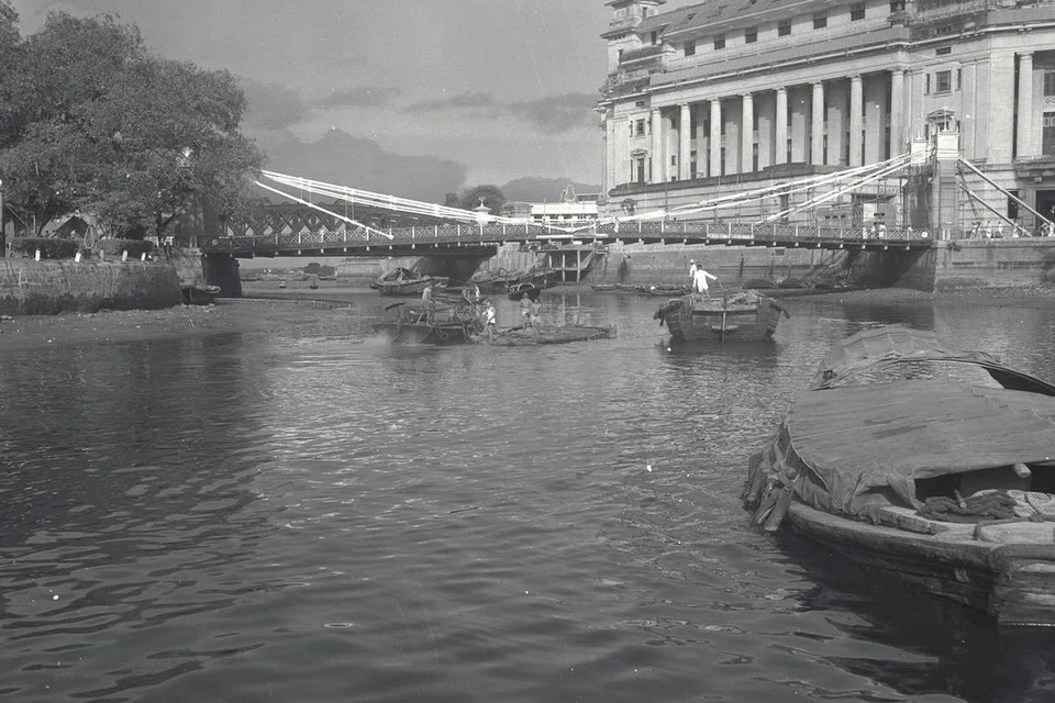 SUNGAI SIBUK: Gambar yang dipetik sekitar 1950-an ini menunjukkan pekerja yang sedang cuba menyelamatkan kargo daripada bot yang karam di Sungai Singapura. Gambar tersebut turut memaparkan Jambatan Cavenagh dan Bangunan Fullerton. 