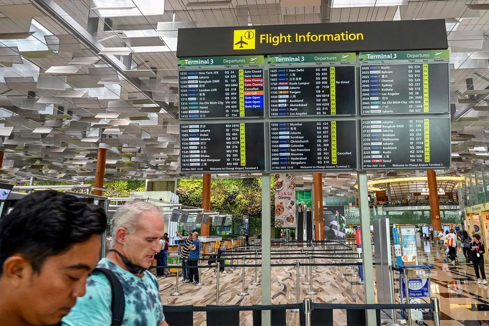 Orang ramai berjalan melepasi papan maklumat yang memaparkan penerbangan Singapore Airlines SQ318 ke London Heathrow yang dibatalkan, di Lapangan Terbang Changi pada 21 Mac 2025.