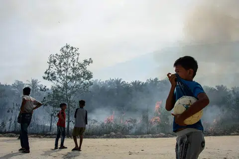 Kanak-kanak memerhati kebakaran hutan di Karya Indah, wilayah Riau pada 19 Julai 2025. 