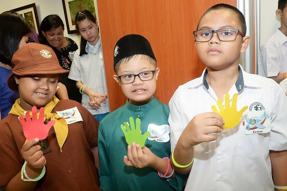 LAMBANG PENYATUAN: (Dari kiri) Nurnatisha Abdul Halim Moulasa dan Elfie Rifaie Nur Nazrul, kedua-duanya dari Sekolah Fernvale Gardens Minds, bersama Eaman Haydrian dari Sekolah Rendah Fernvale, dalam kegiatan menampal pelekat tangan pada papan tanda sempena Hari Sindrom Down Sedunia. - Foto JOHARI RAHMAT