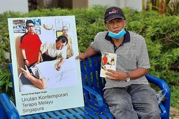 BUKU TERAPI MELAYU: Encik Saini Salleh, seorang mantan wartawan Berita Harian, bersama poster buku 'Urutan Kontemporari Terapis Melayu Singapura' yang ditulis beliau. - Foto ihsan HAJI ABDUL LATIFF AHMAD