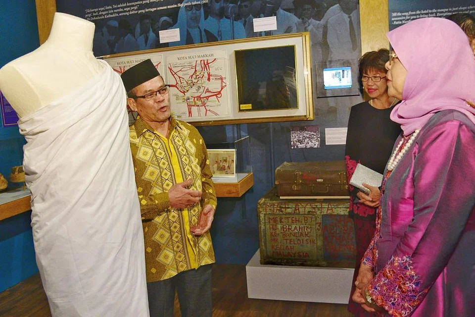 TINJAU PAMERAN HAJI: Presiden Halimah Yacob (kanan) mendengar penerangan Encik Abdul Halim Mohd Amin, konsultan haji bersama Majlis Ugama Islam Singapura (Muis), tentang ihram di pameran Undangan ke Baitullah: Kisah Jemaah dari Nusantara Melayu ke Makkah di Taman Warisan Melayu semalam. - Foto BH oleh DESMOND WEE