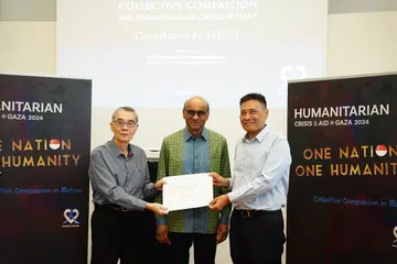 Presiden Dewan Perniagaan dan Perusahaan Melayu Singapura (DPPMS), Encik Abu Bakar Mohd Nor (kanan), menyerahkan cek kepada Duta Kelana dan pengerusi Humanity Matters, Encik Ong Keng Yong (kiri), bagi membantu warga di Gaza pada 10 Mac. Majlis tersebut turut dihadiri Presiden Tharman Shanmugaratnam (tengah).