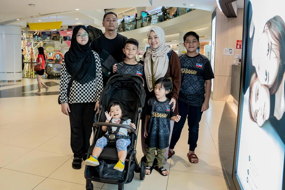 PERSIAPAN TAHUN DEPAN: Antara pengunjung di Tampines Mall ialah Cik Nurul Huda Hasbullah (dua dari kanan, bertudung) dan Encik Muhammad Faizal Zakaria (dua dari kiri, berdiri belakang) kededua berusia 41 tahun, yang mendapat barangan keperluan untuk lima anak mereka sebagai persiapan sempena pembukaan semula sekolah, sebelum kenaikan Cukai Barangan dan Perkhidmatan (GST) dari 8 peratus kepada 9 peratus pada 1 Januari.