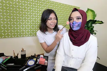 SOLEKAN KESAN KHAS: Jurusolek bebas, Cik Athirah Khairwan, melakukan solekan kesan khas ke atas wartawan, Cik Natasha Mustafa, yang berupa pelitup siap dengan ikon-ikon Singapura khas untuk 'The BM Show' sempena Hari Kebangsaan Singapura ke-55. - Foto BH oleh NUR HUMAIRA SAJAT