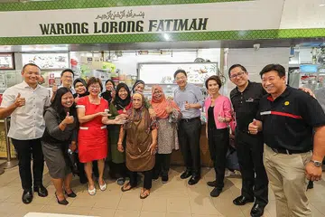 BAUCAR CDC: Encik Fahmi (paling kiri) bersama Timbalan Perdana Menteri, Encik Lawrence Wong (empat dari kanan), serta mayor dan Anggota Parlimen lain serta pegerai di sebuah gerai di pusat penjaja Kampong Admiralty sempena pelancaran Skim Baucar CDC 2023. - Foto MCI