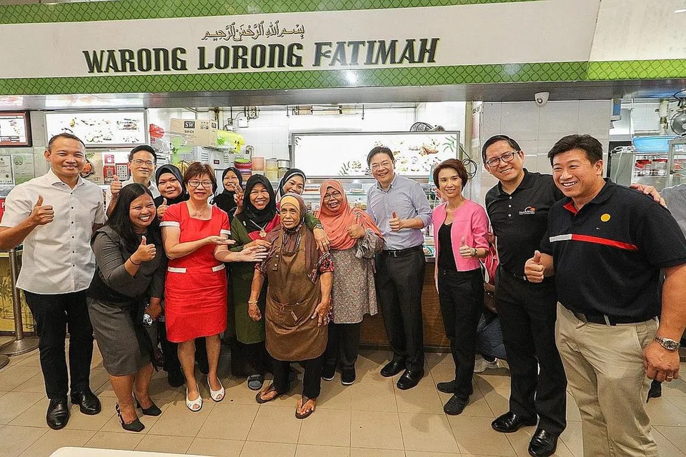 BAUCAR CDC: Encik Fahmi (paling kiri) bersama Timbalan Perdana Menteri, Encik Lawrence Wong (empat dari kanan), serta mayor dan Anggota Parlimen lain serta pegerai di sebuah gerai di pusat penjaja Kampong Admiralty sempena pelancaran Skim Baucar CDC 2023. - Foto MCI