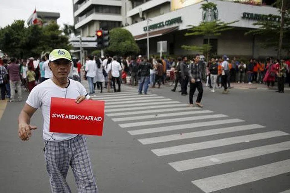 MAHU TERUSKAN KEHIDUPAN SEPERTI BIASA: Seorang penduduk setempat memegang sepanduk yang bermaksud "Kami tidak gentar" di jalan raya yang sibuk seperti biasa semalam di depan kafe Starbucks dekat pusat beli-belah Sarinah Mall, Jakarta, yang merupakan antara lokasi letupan kelmarin. - Foto REUTERS
