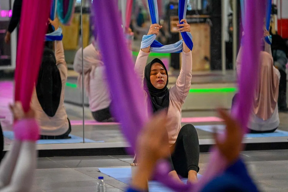 Anggota wanita berlatih yoga udara dalam sebuah sesi di pusat gimnasium khusus wanita di Banda Aceh pada 19 Julai 2025 sedang pemerintah Jakarta mewajibkan  senaman kecergasan setiap hari Jumaat untuk penjawat awam.