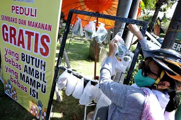 SALING PEDULI: Seorang wanita yang mengenakan pelitup mengambil bungkusan keperluan harian di tengah-tengah lonjakan jangkitan koronavirus di Denpasar, Bali, Indonesia, kelmarin. - Foto REUTERS