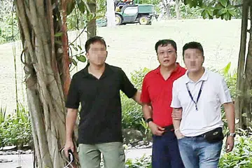 DIDAPATI BERSALAH: Leslie Khoo (berbaju merah) dibawa ke tempat kejadian di Gardens by the Bay selepas ditangkap pada 2016.