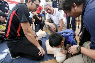 BERSEDIA HADAPI KECEMASAN: Encik Teo (berbaju putih) menyaksikan seorang kanak-kanak lelaki memberi bantuan pernafasan kecemasan di Hari Kesediaan Kecemasan Pasir Ris West semalam. - Foto ZAOBAO