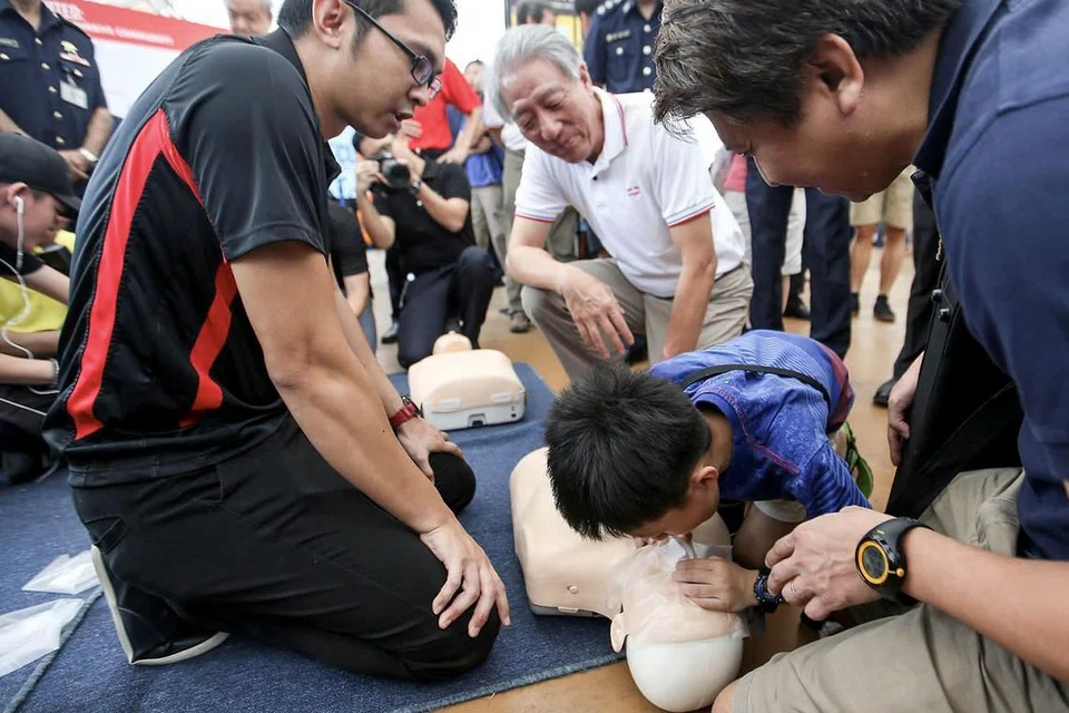 BERSEDIA HADAPI KECEMASAN: Encik Teo (berbaju putih) menyaksikan seorang kanak-kanak lelaki memberi bantuan pernafasan kecemasan di Hari Kesediaan Kecemasan Pasir Ris West semalam. - Foto ZAOBAO