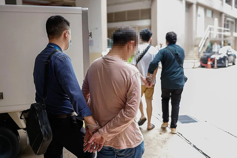 OPERASI PENGUATKUASAAN: Pegawai MOM mengiringi suspek berhubung siasatan melibatkan sindiket yang disyaki membawa masuk warga asing secara haram. - Foto MOM