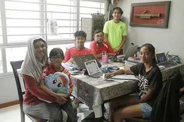 KONGSI RUANG KERJA: Bagi memastikan jadual kelas dalam talian dipatuhi anak-anaknya serta disiplin mereka dijamin, Cik Noraini Mas Noraini Wahid tidak mengizinkan anaknya belajar di bilik sendiri dan hanya duduk di meja makan bersama suaminya. - Foto-foto BH oleh AZMI ATHNI