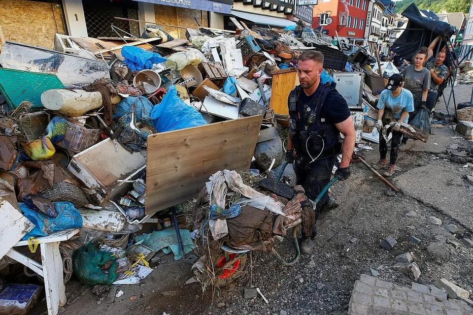 BERAT SAMA DIPIKUL: Seorang anggota polis dan sukarelawan membersihkan sebuah kawasan perumahan, Bad Muenstereifel, yang teruk dilanda hujan lebat dan banjir minggu lalu. - Foto REUTERS