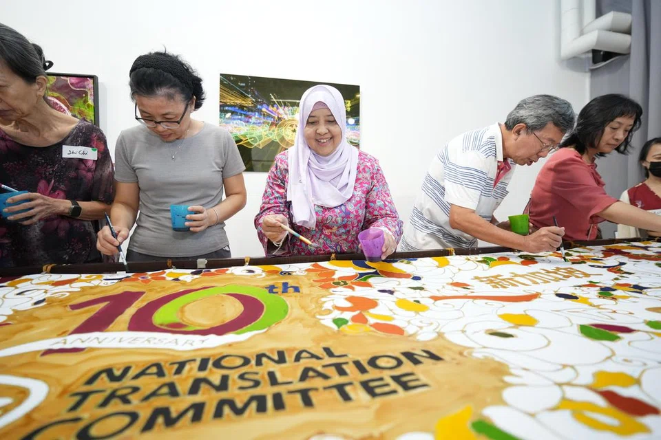 Penterjemah Masyarakat, Cik Sanesa Salleh (bertudung), bersama para penterjemah yang lain sama-sama mewarnakan lukisan batik yang dihasilkan sempena sambutan ulang tahun ke-10 Jawatankuasa Penterjemahan Nasional (NTC) semasa satu sesi pendekatan sempena Hari Raya yang diadakan di Pusat Seni Kamal di Wisma Geylang Serai pada 4 Mei.
