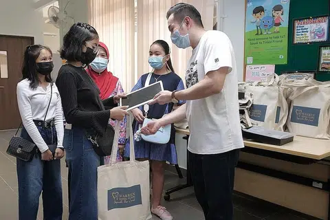 DERMA AMAL: Dr Andy Joshua Warren (kanan), memberi tablet komputer kepada penerima bantuan Persatuan Kanak-Kanak Singapura Nur Darwisyah (berbaju hitam) dan Nur Insyirah (berbaju putih) di cawangan Yishun persatuan itu semalam. Bersama mereka adalah nenek mereka, Cik Siti Rogaiyah (tudung merah). - Foto BH oleh GAVIN FOO