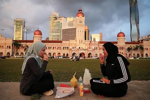 NIKMATI REMANG SENJA: Dua wanita ini berbuka puasa di tengah ibu kota Kuala Lumpur, di Dataran Merdeka, berlatarbelakangkan Bangunan Sultan Abdul Samad yang bersejarah, kelmarin. - Foto REUTERS