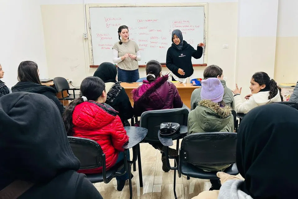SUMBANG MASA: Cik Atikah Syarah Ismail (kanan, berdiri) mengendalikan kelas bahasa Inggeris kepada kanak-kanak pelarian Palestin di Kem Pelarian Al-Fawwar, Hebron, Tebing Barat, bersama seorang lagi sukarelawan.