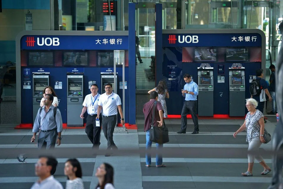 Pekerja pejabat berjalan melewati mesein ATM UOB di Raffles Place.