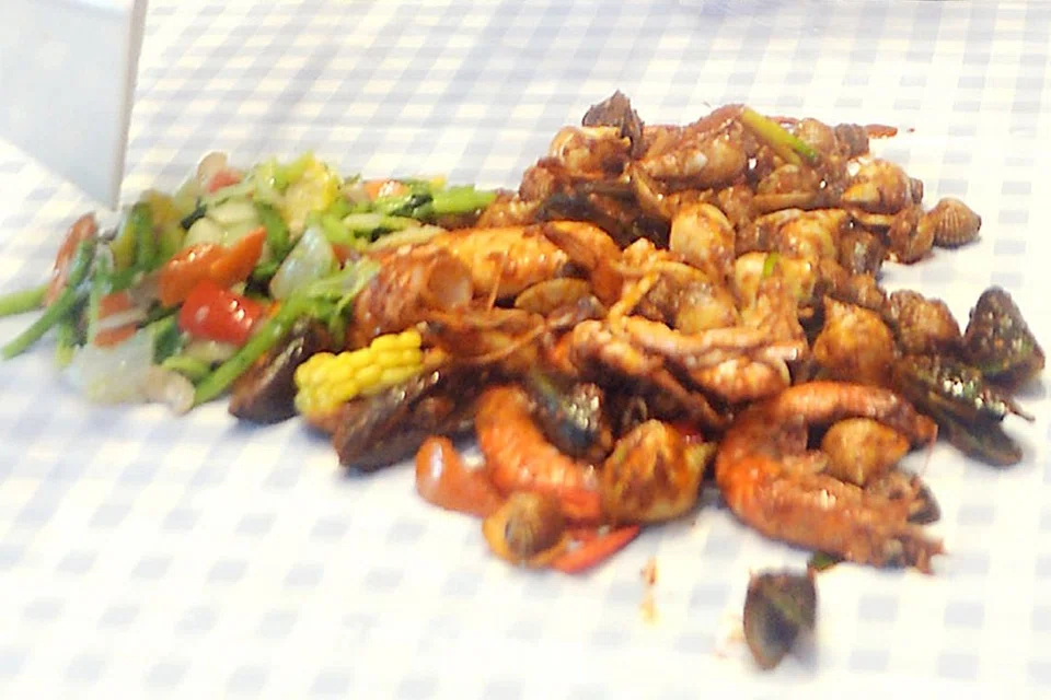 BERSELERAK DI ATAS PLASTIK: Sajian 'shell out' biasanya dimakan secara beramai-ramai selepas semua bahan makanan laut yang telah dimasak ditabur di atas plastik di atas meja. - Foto fail 