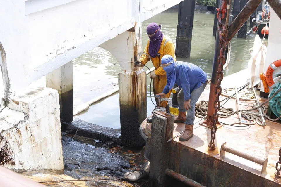 KERJA PEMBERSIHAN DITERUSKAN: Pekerja daripada Singapore Oil Spill Response Centre Pte Ltd menggunakan bahan penyebar untuk mencairkan minyak di permukaan batu bata di Terminal Feri Changi Point. - Foto FARAH REZAL