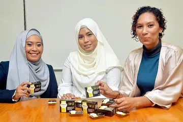 TEMBUSI PASARAN EKSPORT: (Dari kiri) Cik Masturah dengan rakan niaganya, Cik Nurlela, menunjukkan produk sabun yang dihasilkan mereka, sambil diperhatikan Cik Aida. - Foto KHALID BABA