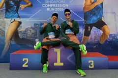Encik Muhammad Dani Mirza Ahmad Affandi (kiri) dan Encik Muhamad Nurirsyad Azman bergambar di podium setelah selesai berlari dalam acara separuh maraton sejauh 21.1 kilometer, 2XU Compression Run 2026, dengan berbaju Melayu lengkap dengan samping dan songkok.