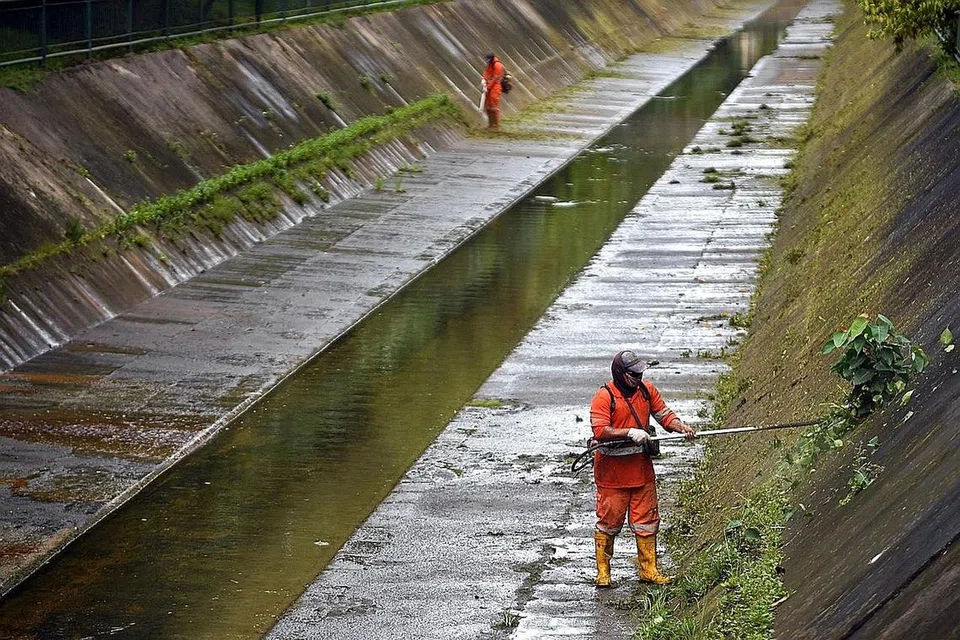 TERUSAN UNTUK LANCARKAN PENGALIRAN AIR: Pekerja memotong rumput di dalam terusan air di Sungai Serangoon pada Disember tahun lalu. Terusan besar ini membantu mengelakkan banjir daripada berlaku. - Foto BH oleh LIM YAOHUI