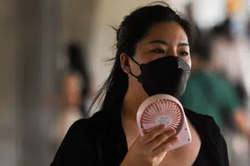 FAEDAH KIPAS MINI: Seorang wanita di Bangkok menggunakan kipas mini untuk menyejukkan diri. - Foto 