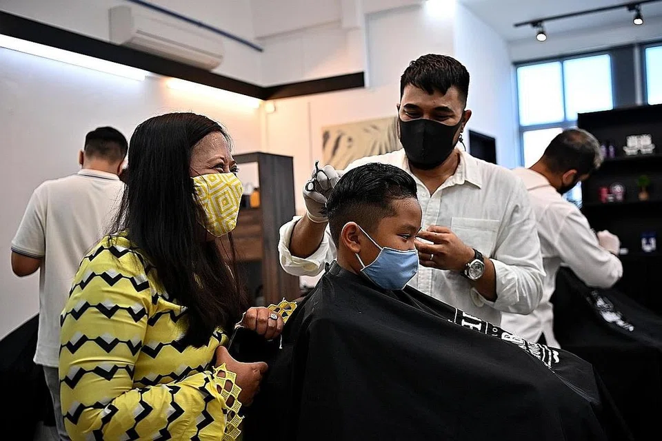 SEBAR KECERIAAN SYAWAL: Cik Mariam (kiri) melihat Darwin Anaqi Airullnizam (tengah), lapan tahun, dapat guntingan rambut percuma dari Encik Noor di Bespoke Barbers & Co. - Foto BH oleh LIM YAO HUI