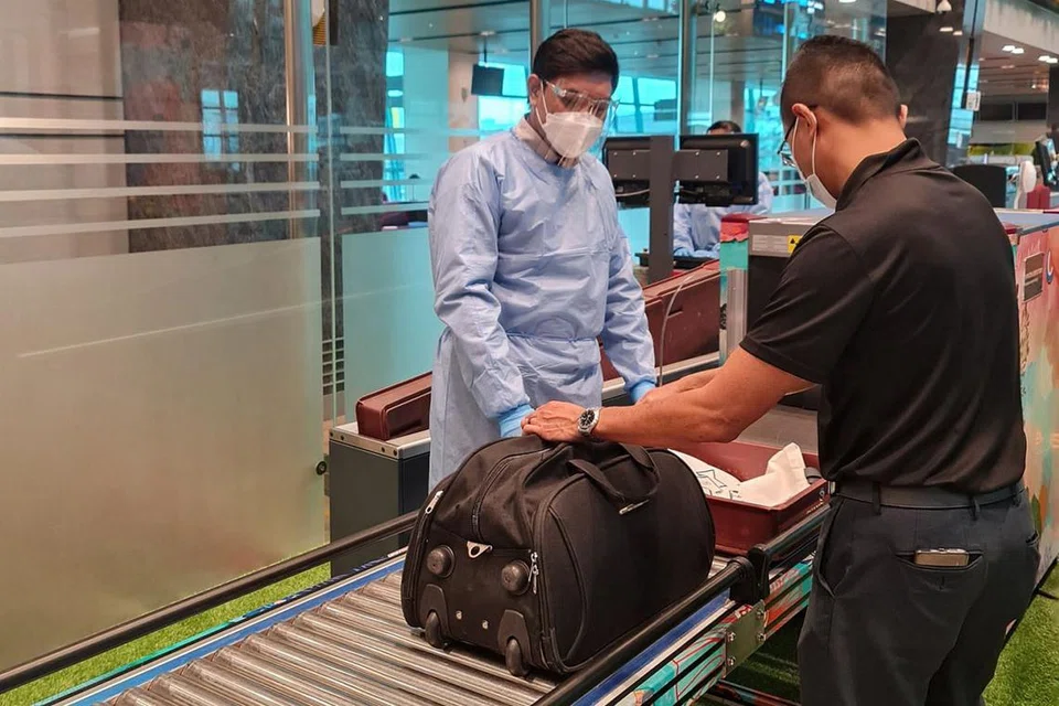 PASTIKAN PENUMPANG SELAMAT: Pegawai keselamatan penerbangan, Encik Ahmad Faiz Amirul Zainuddin, yang memakai PPE melakukan pemeriksaan ke atas seorang penumpang di Terminal 1 sebelum menaiki pesawat. Ini adalah peraturan yang diperketat di Lapangan Terbang Changi. - Foto CERTIS