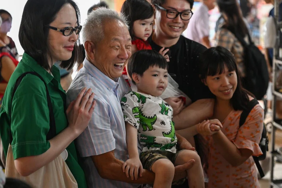 BERAMAH-TAMAH: Bakal calon, usahawan Encik Ng Kok Song (mendudung budak) bergambar dengan pengunjung di pasar dan pusat penjaja Kovan 209 bersama tunangnya, Cik Sybil Lau.