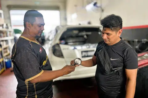 Encik Mohd Azmi Abd Jalil (kiri), menunjukkan alat ganti kenderaan kepada Encik Muhammad Khaleej Mun Chee, di bengkel beliau yang terletak di Larkin, Johor Bahru.
