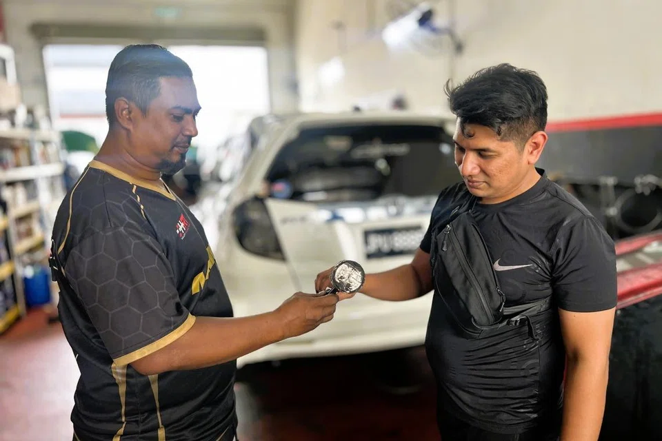 Encik Mohd Azmi Abd Jalil (kiri), menunjukkan alat ganti kenderaan kepada Encik Muhammad Khaleej Mun Chee, di bengkel beliau yang terletak di Larkin, Johor Bahru.
