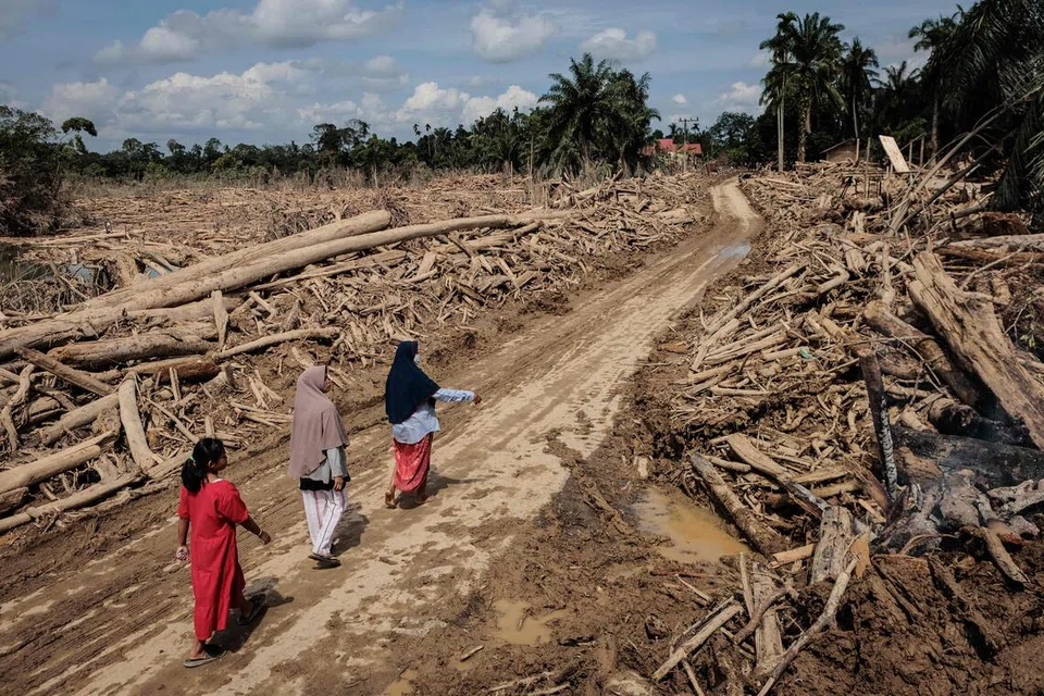 Beberapa wanita berjalan di atas jalan yang telah dibersihkan daripada pokok-pokok tumbang selepas banjir kilat melanda Aceh Tamiang di Sumatera Utara pada 10 Disember 2025.
