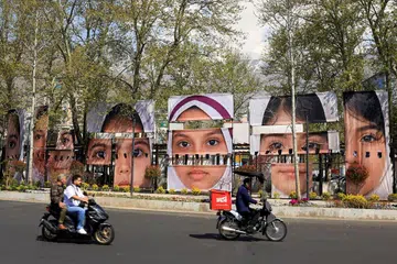 Orang ramai menunggang motosikal di sepanjang jalan melepasi sepanduk yang memaparkan potret pelajar yang terkorban dalam serangan ke atas sebuah sekolah perempuan semasa konflik Amerika-Israel dengan Iran, di tengah gencatan senjata, di Dataran Tajrish, Teheran, Iran pada 15 April 2026. 