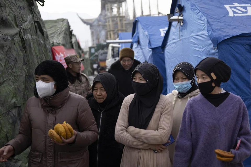 CARI PERLINDUNGAN: Para penduduk wanita membawa makanan yang disediakan oleh sukarelawan di sebuah kem untuk orang-orang yang berpindah akibat gempa bumi di Dahejia, Wilayah Gansu, China, pada 20 Disember. 