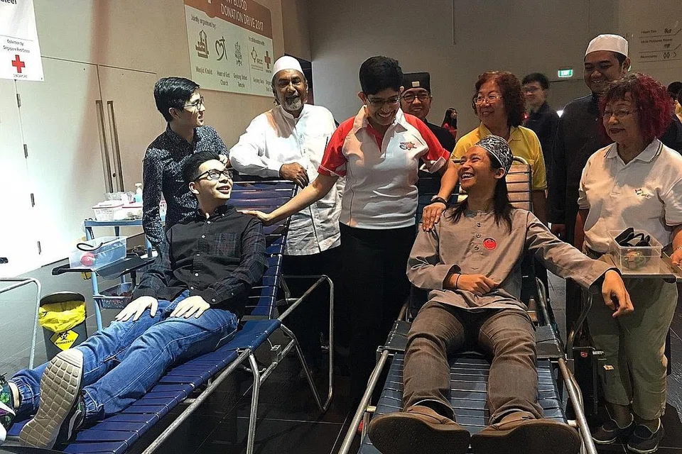 GEMENTAR TUNGGU GILIRAN: Dr Fatimah (tengah) bersembang bersama dua penderma darah (duduk dari kiri) Encik Charleston Lim dan Encik Nadhar Ramli sambil diiringi pemimpin badan agama dari gereja Heart of God Church (HOGC), Masjid Khalid dan Kuil Geylang United. - Foto FAKHRURADZI ISMAIL