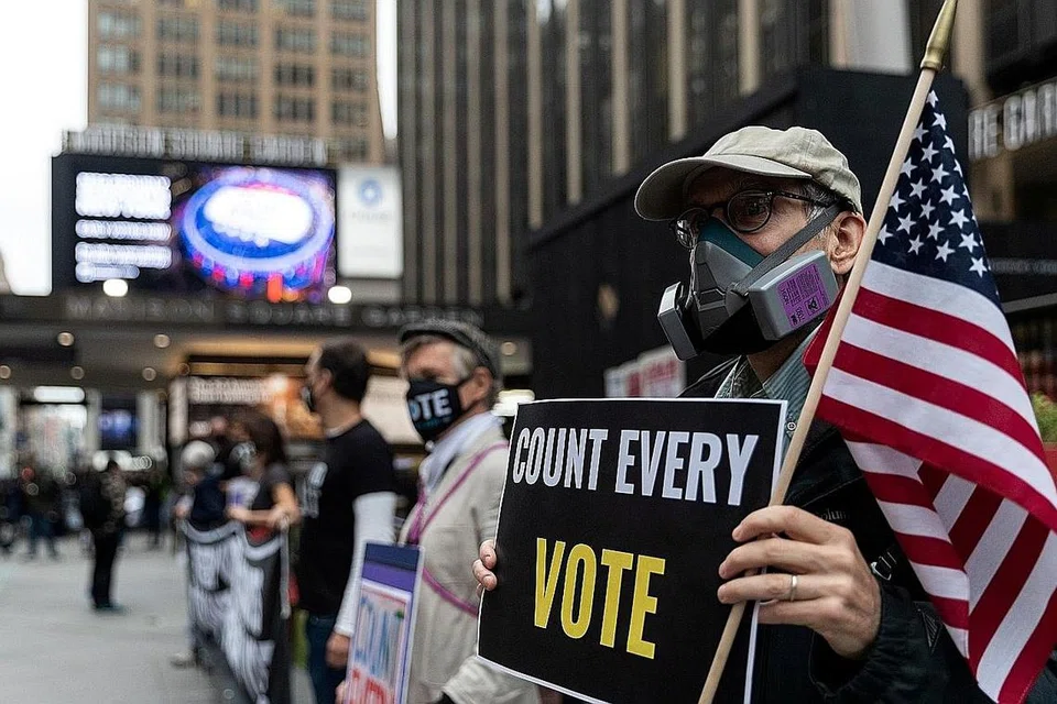 JUMLAH REKOD PENGUNDI: Seorang lelaki memakai topeng pelindung disebabkan pandemik Covid-19, memegang papan tanda di luar Madison Square Garden, yang digunakan sebagai tempat mengundi, pada hari pertama pengundian awal di Manhattan, New York, pada 24 Oktober. Terdapat jumlah rekod pengundi semasa pengundian awal di seluruh Amerika Syarikat dalam pilihan raya presiden antara calon Republik Presiden Donald J. Trump dan calon Demokrat mantan naib presiden Joe Biden. - Foto REUTERS 