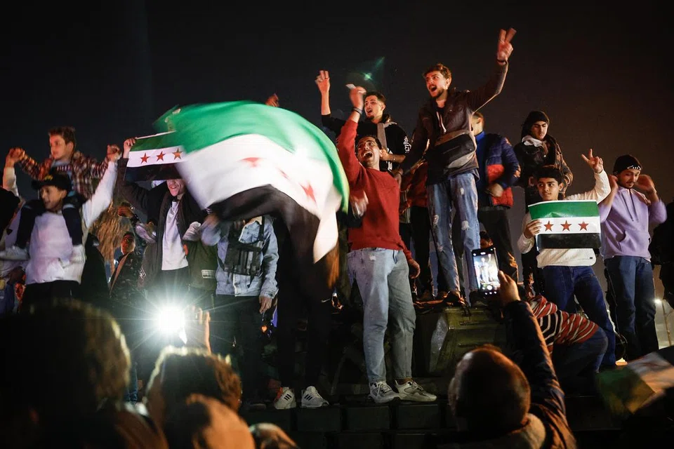 Rakyat Syria mengibarkan bendera tiga bintang pembangkang ketika mereka meraikan kejatuhan rejim Bashar al-Assad di Dataran Umayyad pada 11 Disember, hari perintah berkurung ditarik balik di Syria.