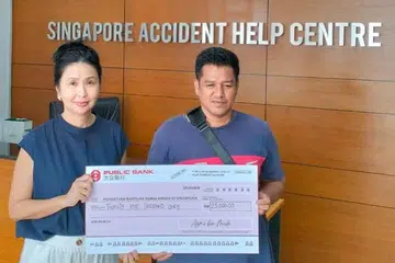Atas bantuan yang diberikan kepadanya, Encik Azmi Muda (kanan)  memberi sumbangan RM25,000 ($7,765) kepada Pusat Bantuan Kemalangan Singapura (SAHC) Johor pada 26 September 2024. Menerima cek simbolik tersebut adalah Ketua Pegawai Eksekutif SAHC Johor, Cik Janey Wong (kiri).