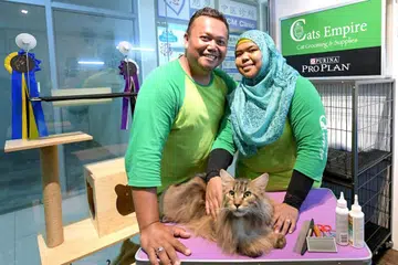 BERMULA DARI MINAT: Pasangan suami isteri Encik Hussein Masor (kiri) dan Cik Fadilah Ismail membuka kedai khidmat penjagaan khusus buat kucing dua tahun lepas dan kini bercadang mahu mengembangkan perniagaan mereka kepada bidang fotografi kucing. Bersama mereka ialah salah satu dari kucing mereka, Toshi. - Foto BH oleh NG SOR LUAN