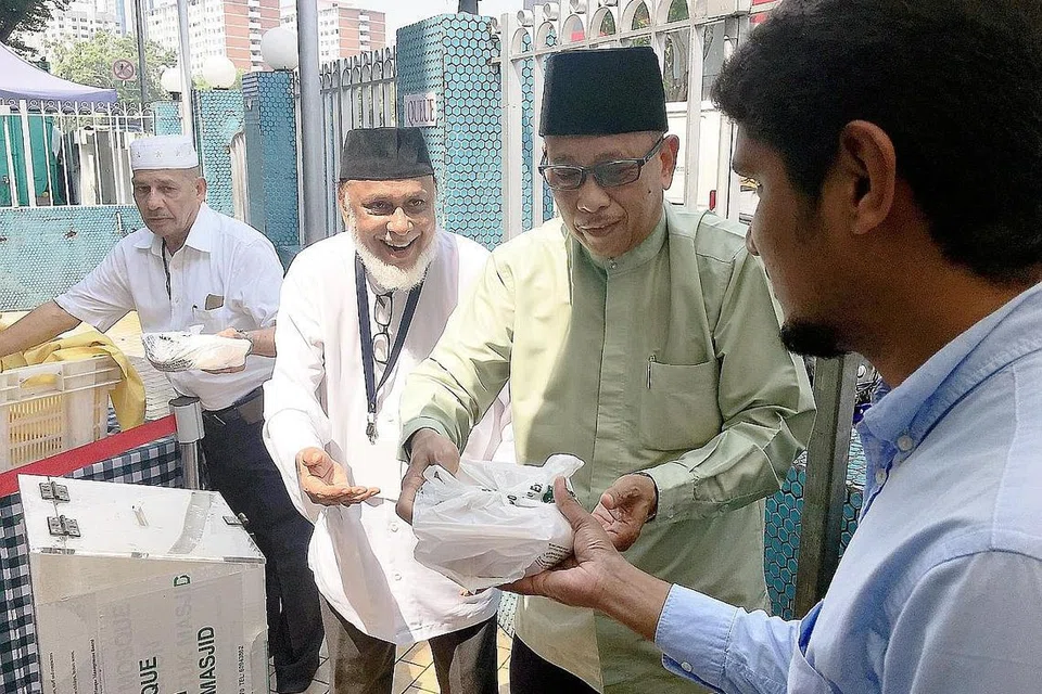 ACARA TAHUNAN: Pengurus Besar Kelompok Masjid Utara Tengah, Haji Paiman Supangat (berkaca mata); bersama Haji Osman (dua dari kiri); dan Naib Pengerusi Masjid Malabar, Haji Sulaiman Kuriya Abdulla (kiri), mengagihkan nasi beriani kepada salah seorang jemaah masjid selepas solat Jumaat semalam. - Foto FAKHRURADZI ISMAIL