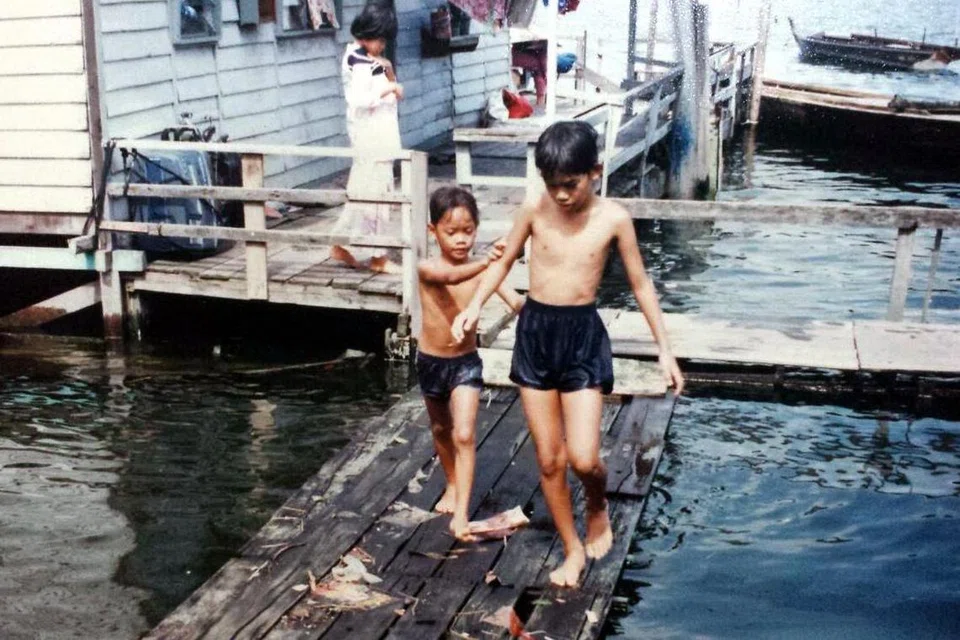 Kanak-kanak bermain di papan kayu yang menghubungkan rumah-rumah atas air di Kampong Lorong Fatimah ketika air pasang pada awal 1970-an.